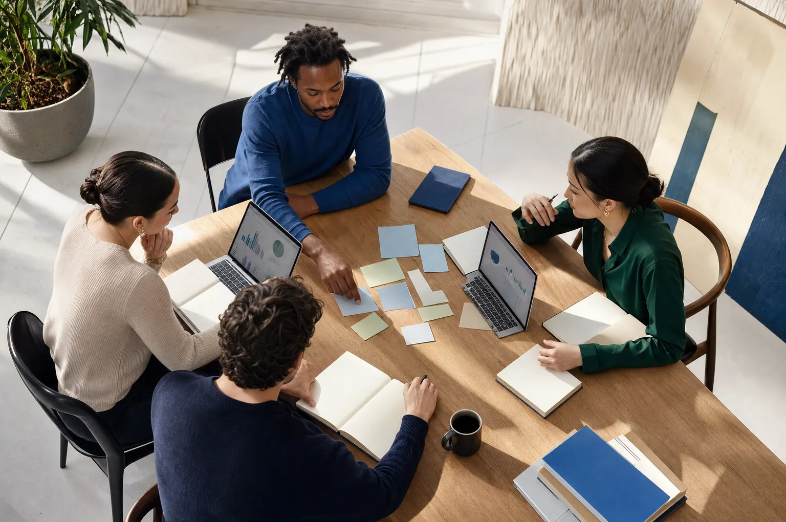 Four colleagues collaborate around a wooden table with laptops and sticky notes, demonstrating how CAQA CRM supports.