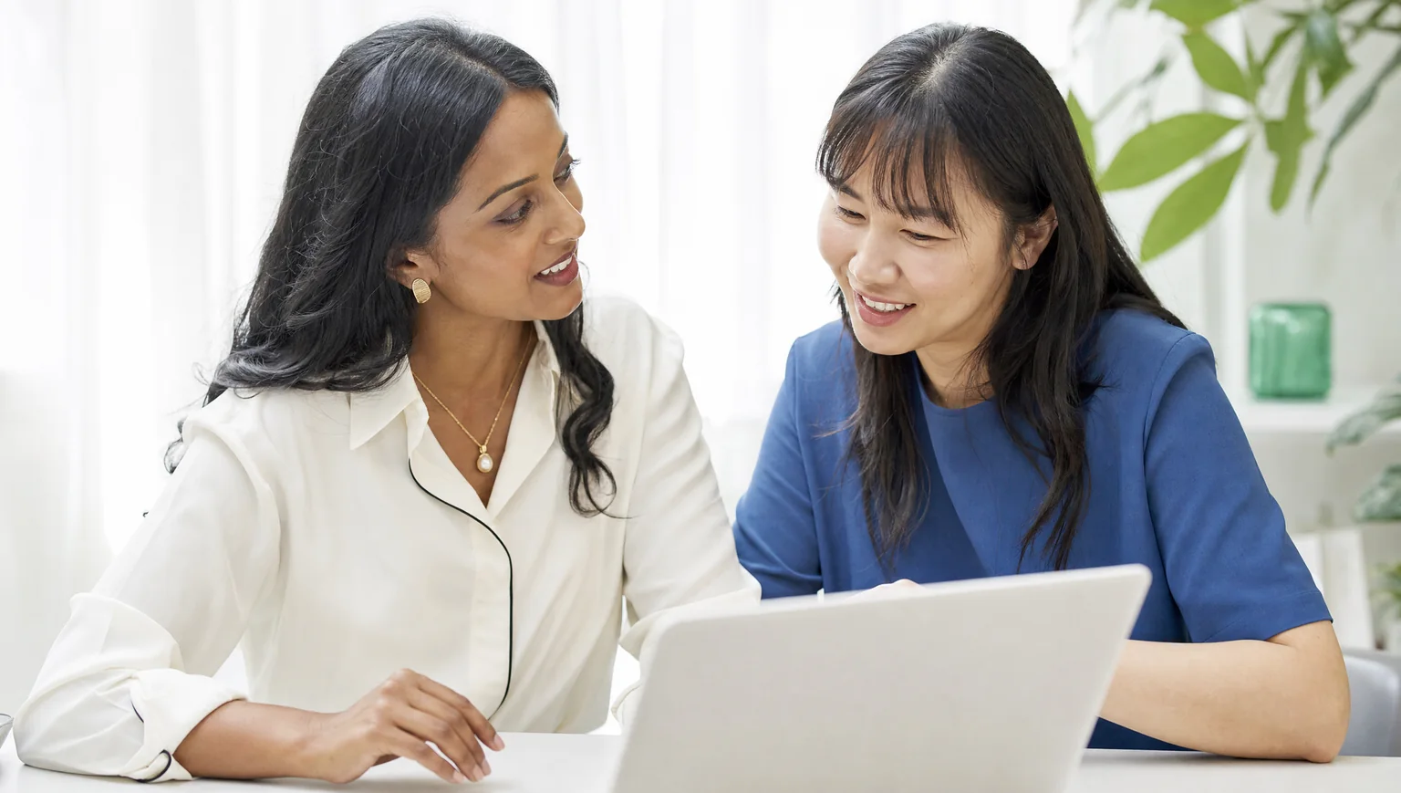 Two businesswomen collaborate on a laptop, demonstrating how CAQA CRM supports teamwork and connection.
